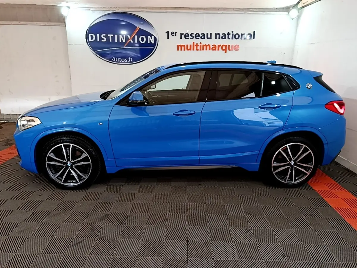 BMW X2 sDrive20i M Sport bleu en vue profil droit dans un showroom avec jantes alliage et toit noir.