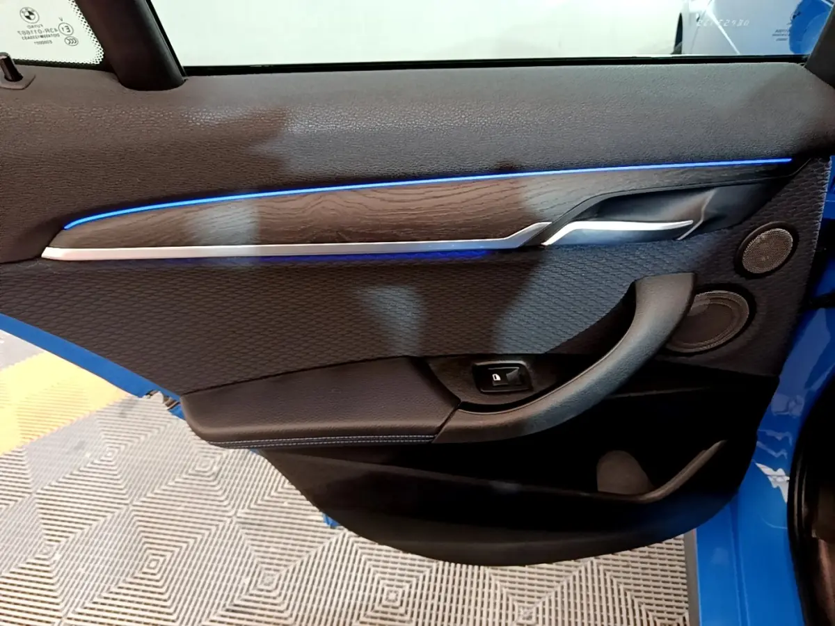 Gros plan sur la porte intérieure côté gauche du BMW X2 bleu, avec éclairage d’ambiance bleu et garniture bois.
