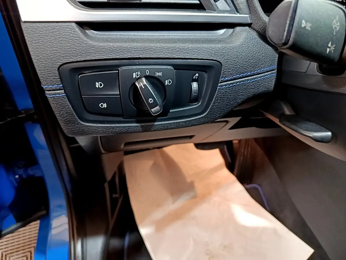 Détail du panneau de commande des phares côté gauche d’un BMW X2 bleu, avec surpiqûres bleues visibles.