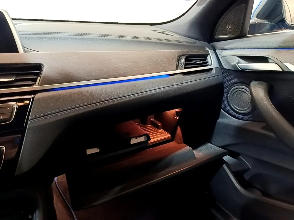 Intérieur côté passager du BMW X2 bleu, tableau de bord avec éclairage d'ambiance bleu et boîte à gants ouverte.
