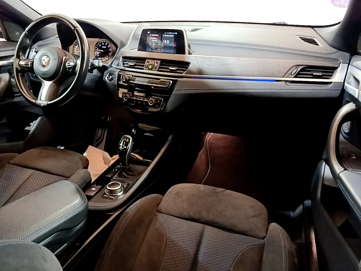 Intérieur BMW X2 sDrive20i M Sport 2019, vue avant côté conducteur, tableau de bord avec écran tactile et éclairage d’ambiance bleu.