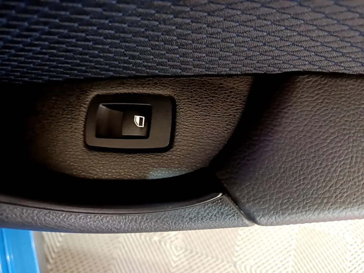 Gros plan sur le bouton de lève-vitre dans la portière intérieure noire d'une BMW X2 bleu sDrive20i M Sport.