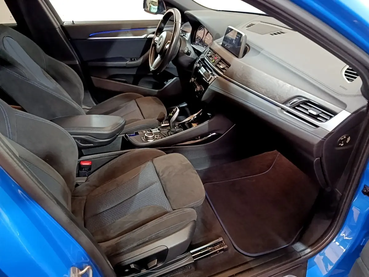 Vue intérieure côté passager avant d'une BMW X2 sDrive20i M Sport bleu, avec sièges en alcantara et tableau de bord moderne.