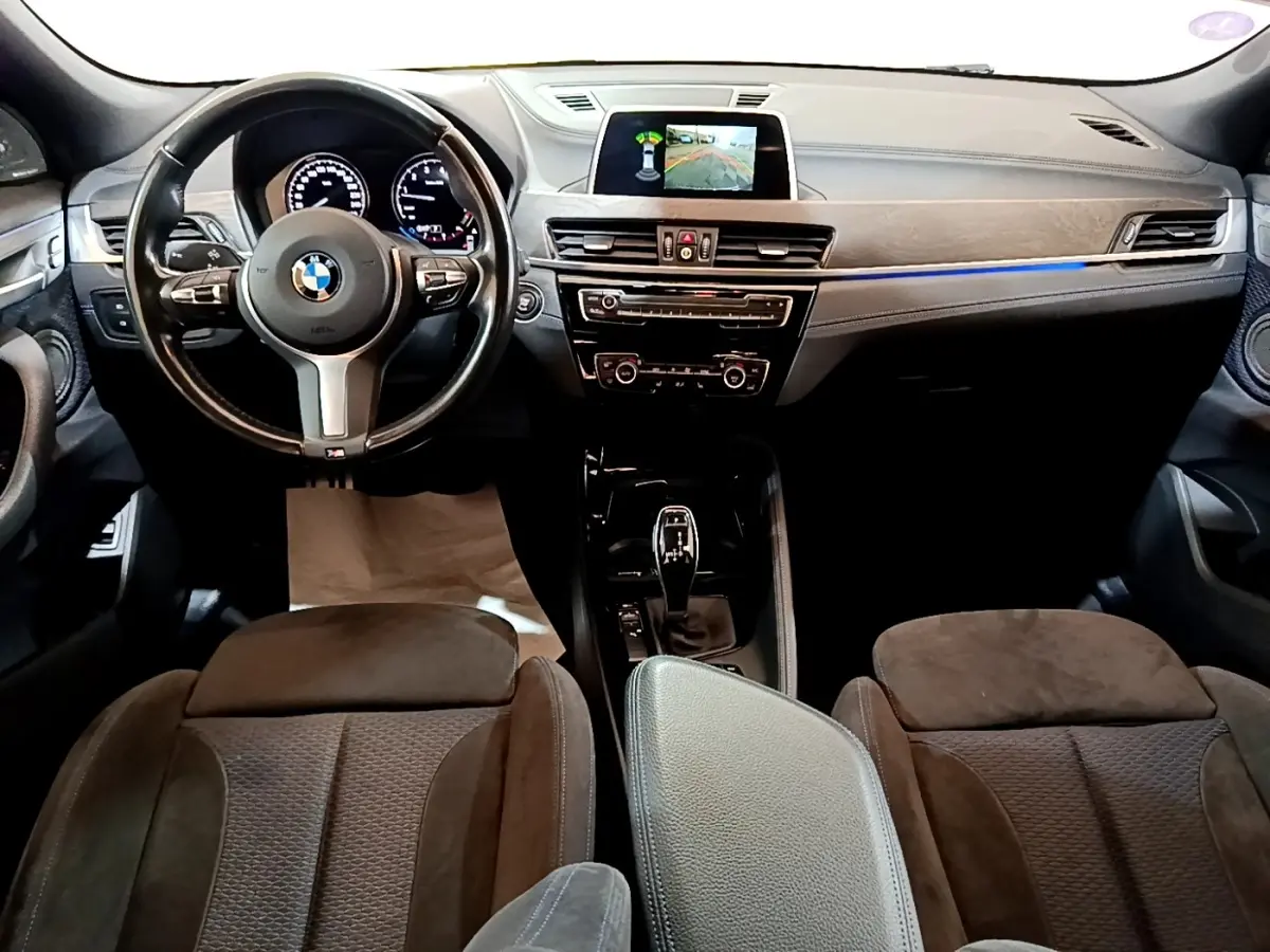Vue intérieure avant de la BMW X2 sDrive20i M Sport 2019, tableau de bord noir avec écran tactile et volant cuir.