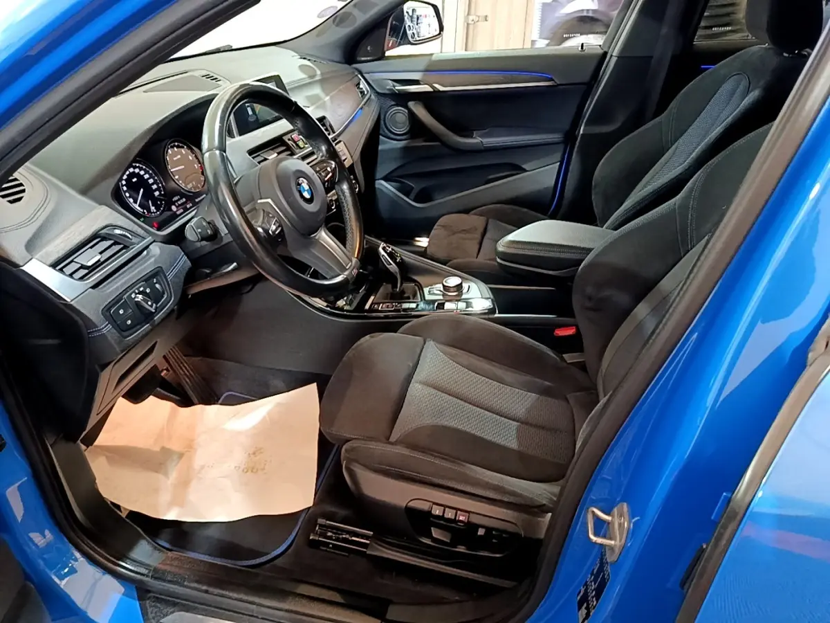 Vue intérieure côté conducteur d'une BMW X2 sDrive20i M Sport bleu avec sièges noirs et tableau de bord moderne.