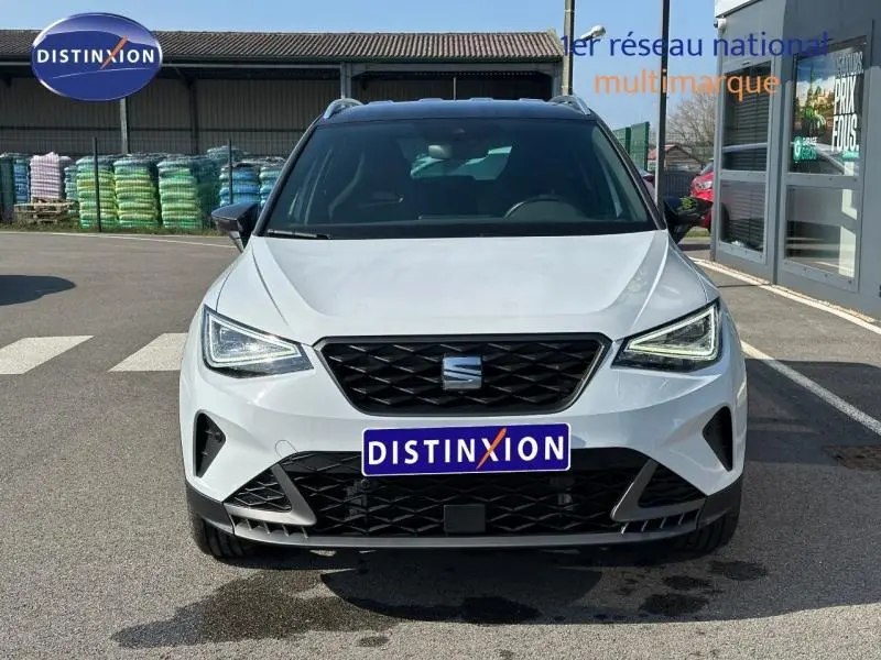 Vue frontale d'un SEAT Arona 2025 blanc Candy avec toit noir Minuit, calandre noire et phares LED allumés.