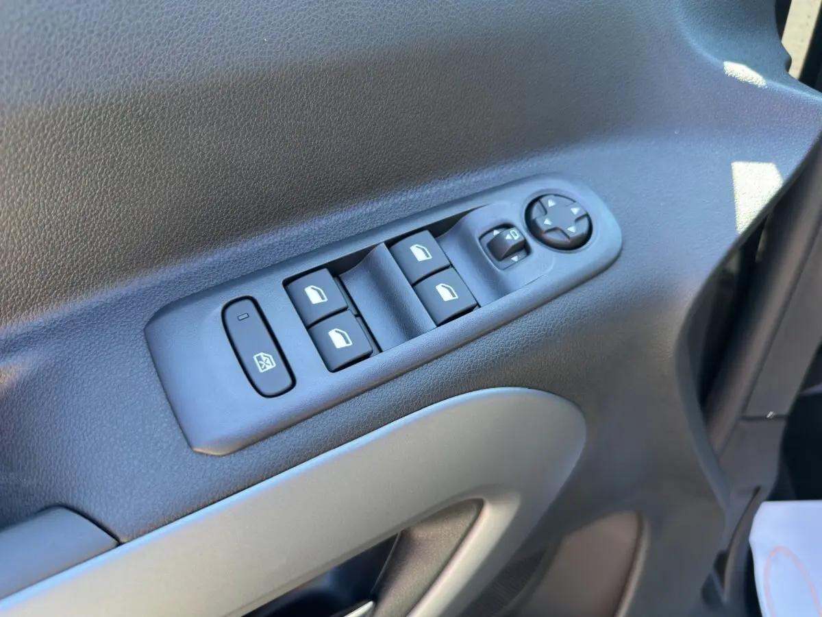 Gros plan sur les commandes des vitres électriques et rétroviseurs sur la portière côté gauche du Citroën Berlingo noir 2026.