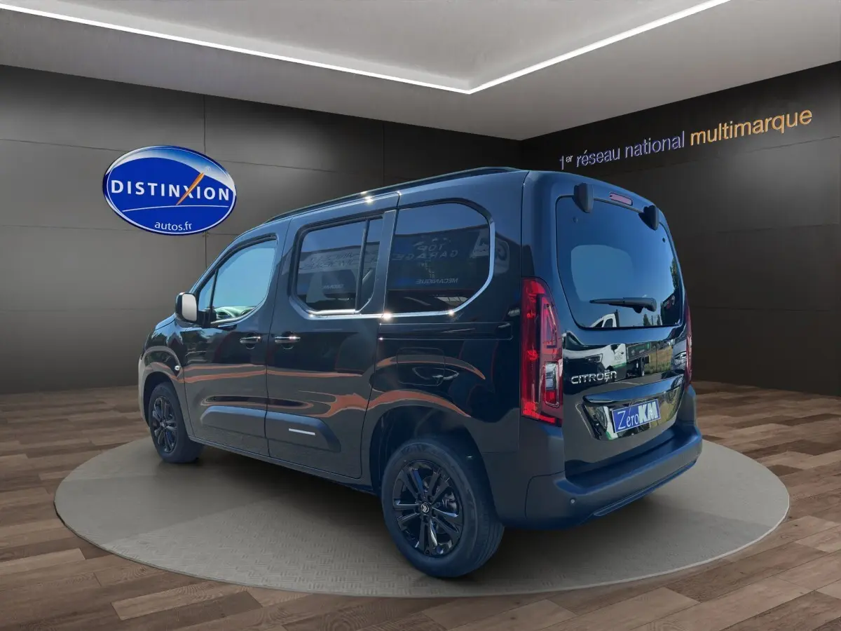 Citroën Berlingo noir vu en 3/4 arrière droit, avec vitres teintées et jantes noires dans un showroom.