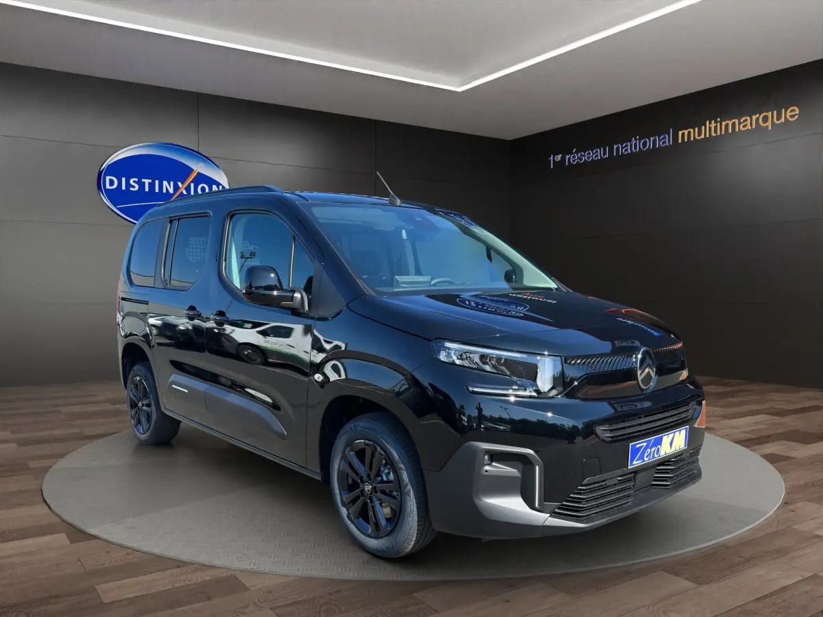 Vue 3/4 avant gauche du Citroën Berlingo noir 2026 avec jantes noires, présenté en showroom intérieur.