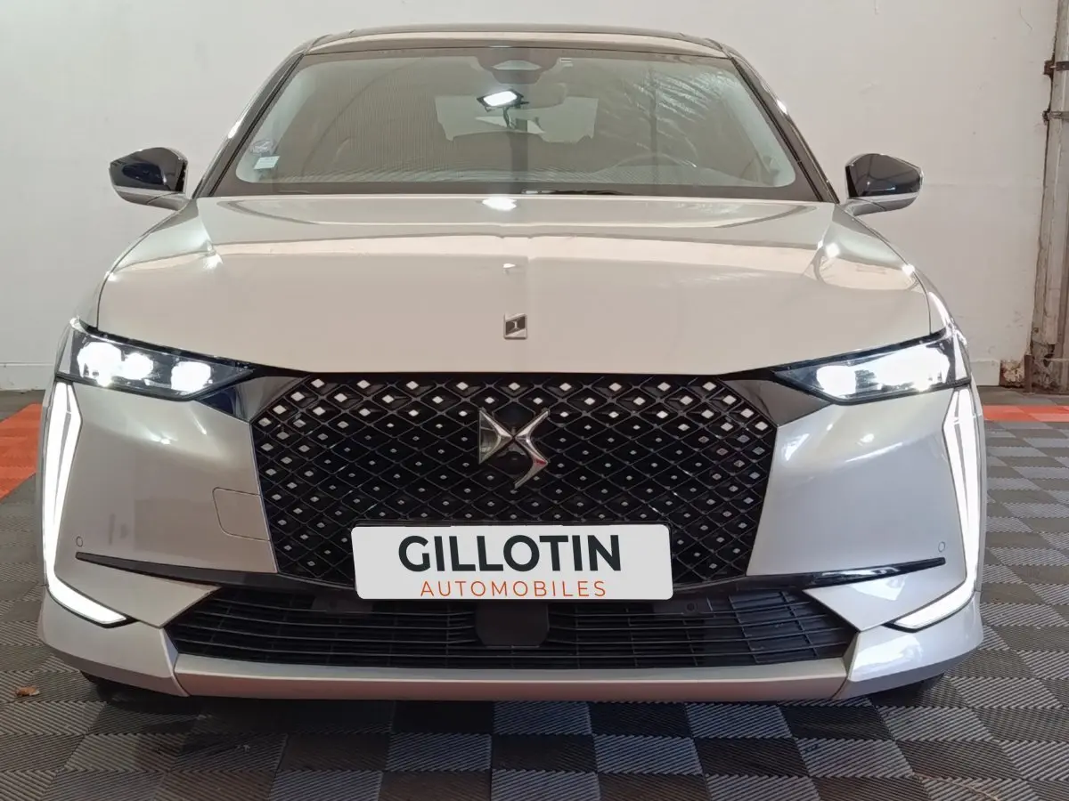 Vue frontale d'une DS4 E-TENSE 225 gris clair avec calandre noire et phares LED allumés dans un garage.