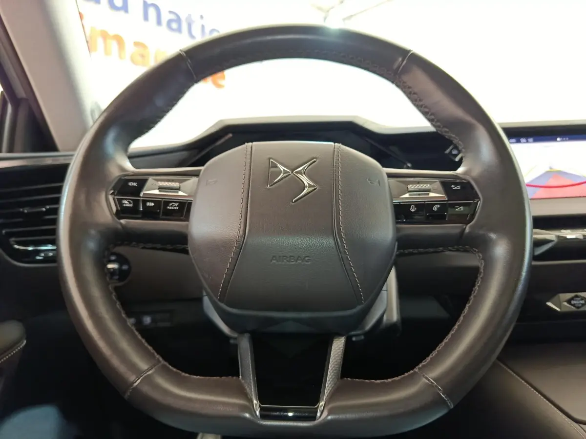 Vue rapprochée du volant cuir noir de la DS4 E-TENSE 225 avec commandes intégrées et tableau de bord numérique.