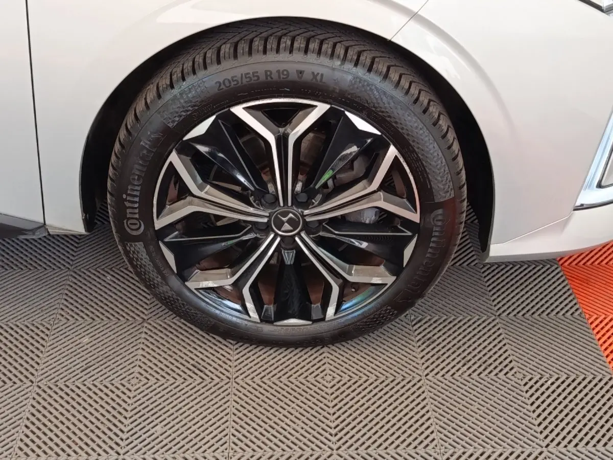 Gros plan sur la roue avant droite d'une DS4 E-TENSE 225 gris clair avec jante noire et argentée au design géométrique.