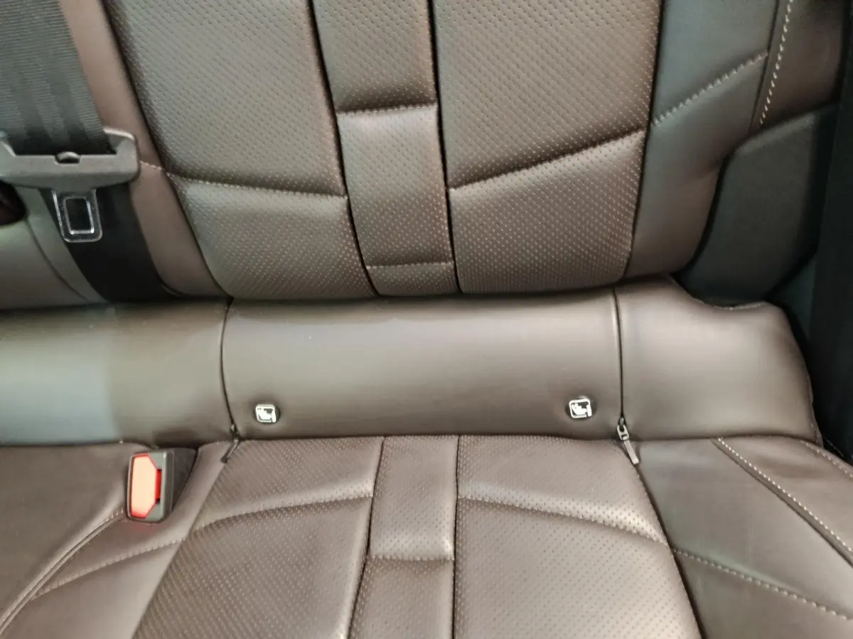 Gros plan sur la banquette arrière en cuir marron perforé du DS4 E-TENSE 225 LA PREMIERE, avec ceintures visibles.