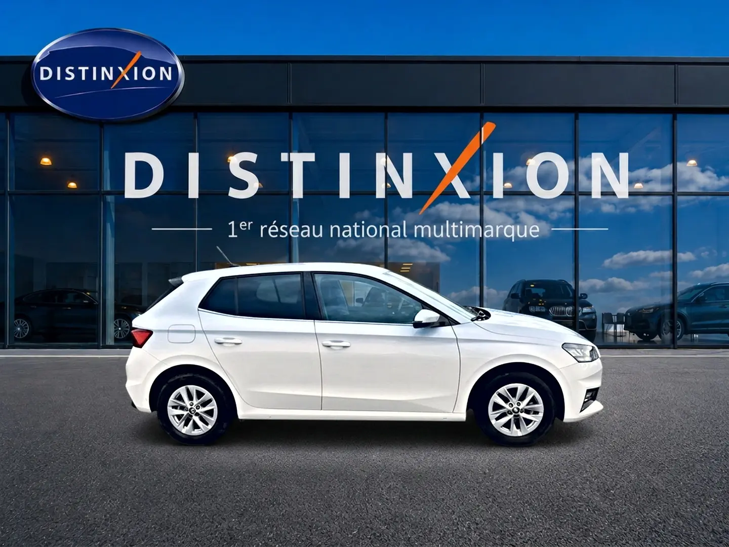 Profil droit d'une Skoda Fabia blanche 2025 garée devant une vitrine avec logo Distinxion.