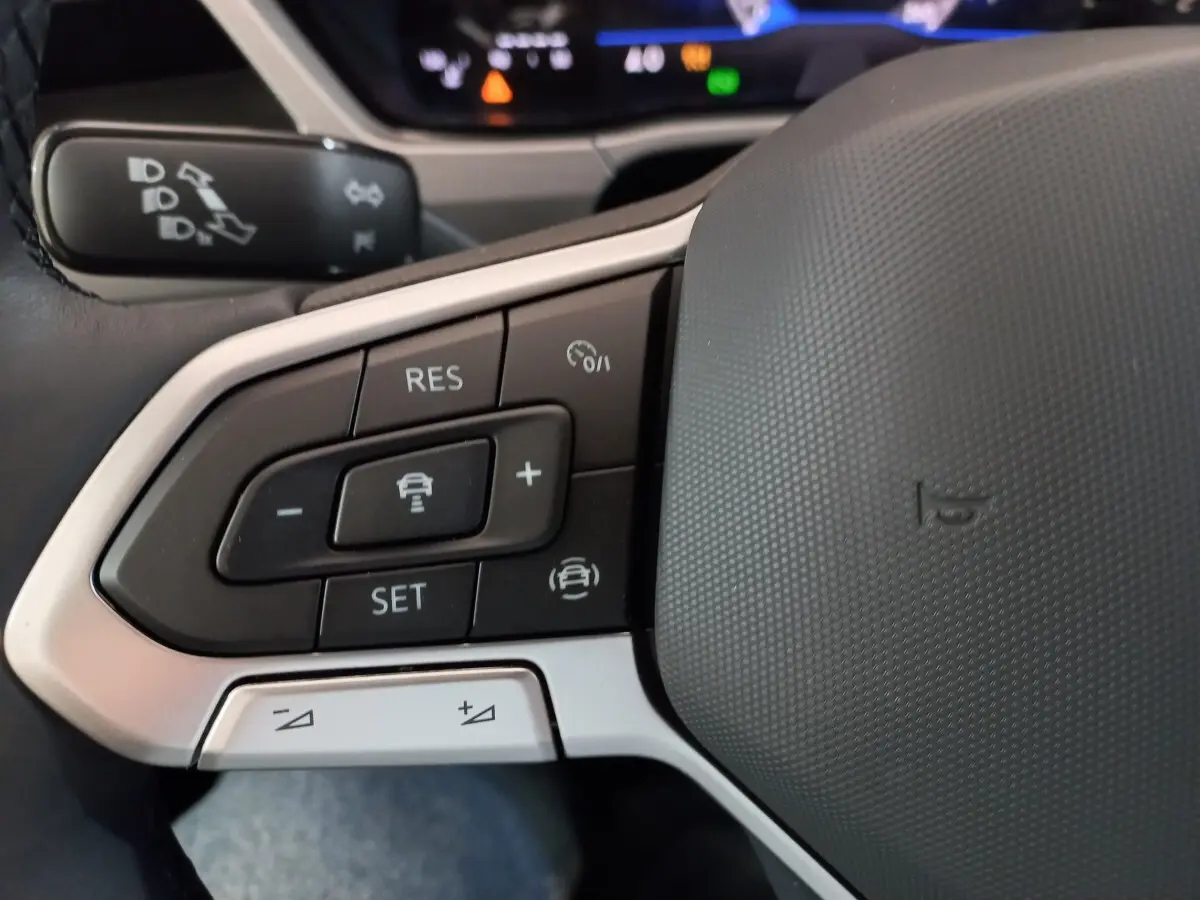 Gros plan sur les commandes de régulateur de vitesse au volant cuir gris du Volkswagen Touran noir 2024.