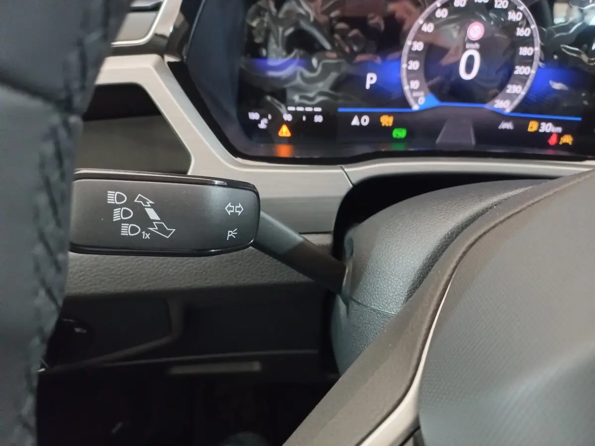 Gros plan sur la manette de clignotant gauche et le combiné d'instruments numérique du Volkswagen Touran 2024 noir.