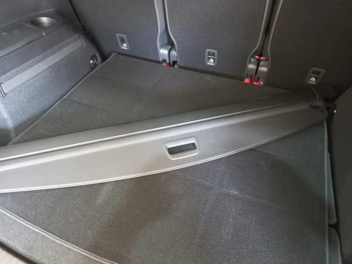Coffre noir du Volkswagen Touran 2024 vu de dessus, avec cache-bagages partiellement déployé et sièges arrière rabattus.