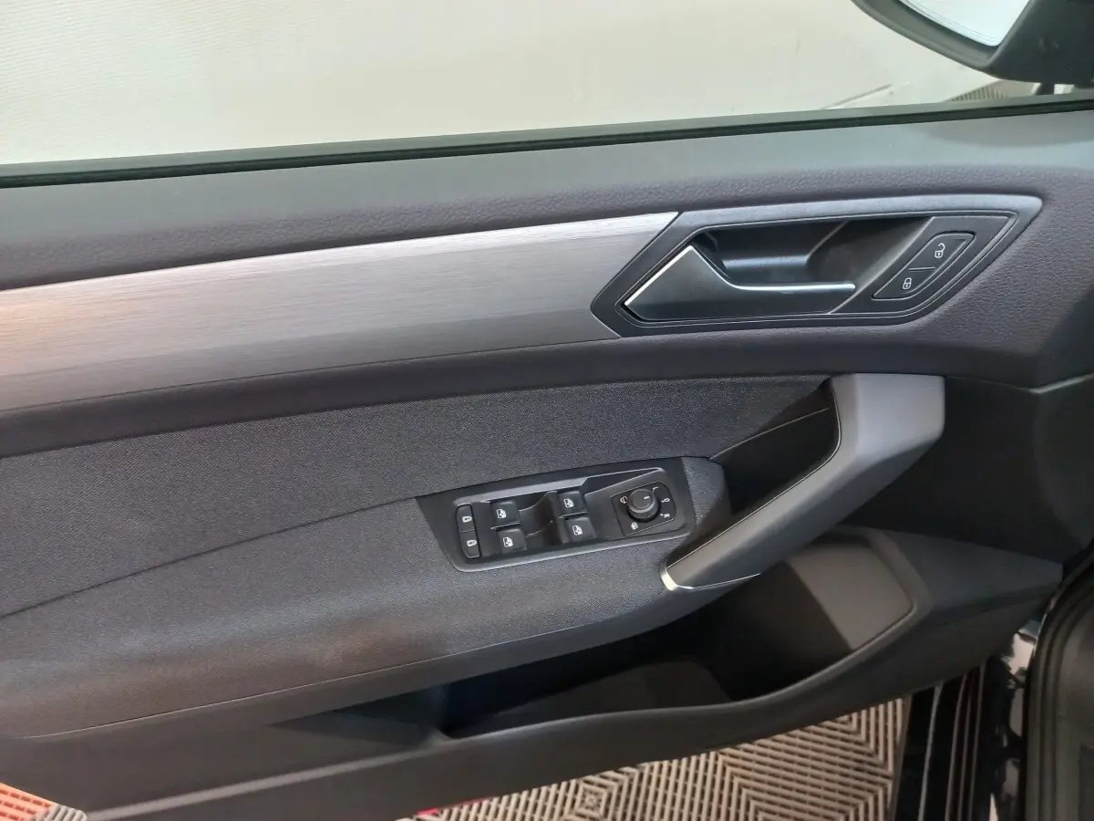 Détail de la porte avant gauche du Volkswagen Touran 2024 noir, avec commandes électriques et insert argenté.