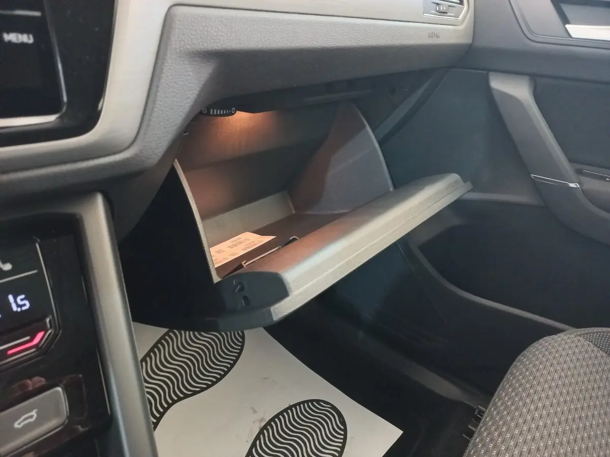 Intérieur du Volkswagen Touran 2024 noir, vue côté passager sur la boîte à gants ouverte avec éclairage intérieur.