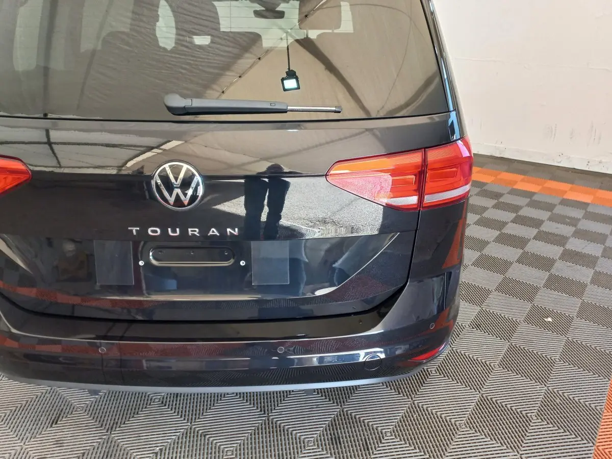 Vue arrière du Volkswagen Touran noir 2024 avec feux rouges et logo VW bien visibles sur fond de sol damier.