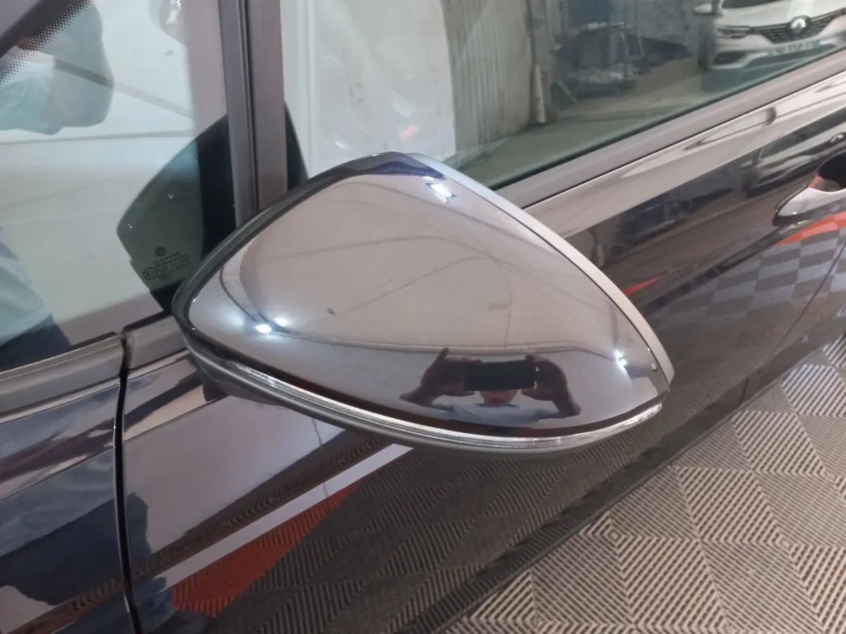 Rétroviseur côté gauche noir brillant du Volkswagen Touran 2024 avec clignotant intégré, vue rapprochée en intérieur.