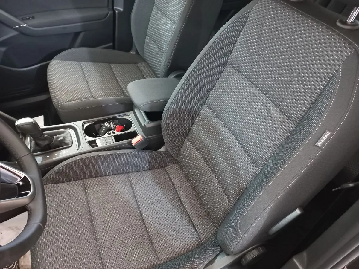 Vue intérieure rapprochée des sièges avant gris foncé du Volkswagen Touran 2024 avec console centrale et levier de boîte automatique.