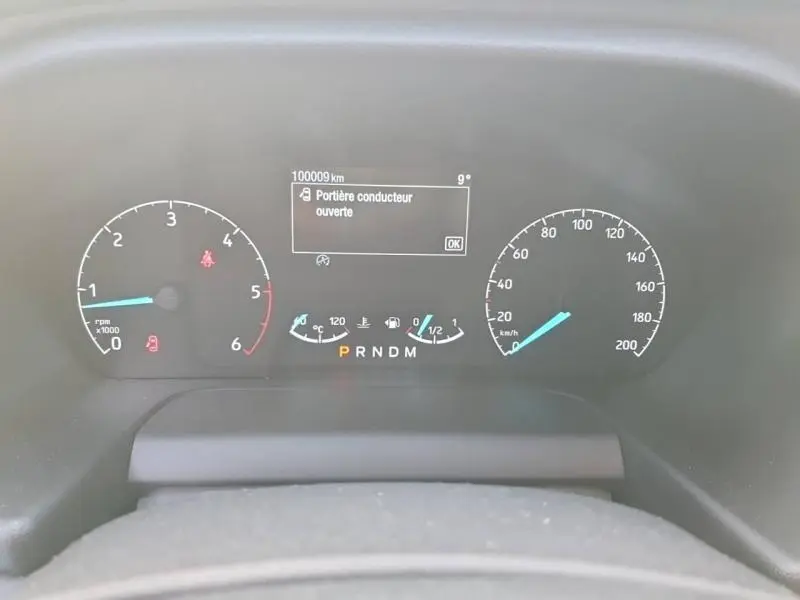 Tableau de bord du Ford Transit Custom blanc, affichant 100009 km et message "Portière conducteur ouverte"