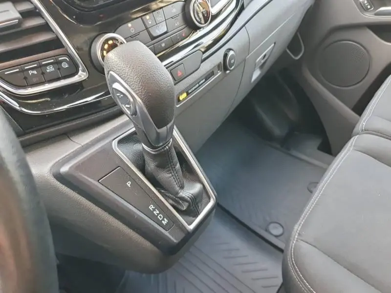 Gros plan sur la console centrale du Ford Transit Custom blanc Glacier, mettant en valeur le levier de vitesses automatique et les commandes.
