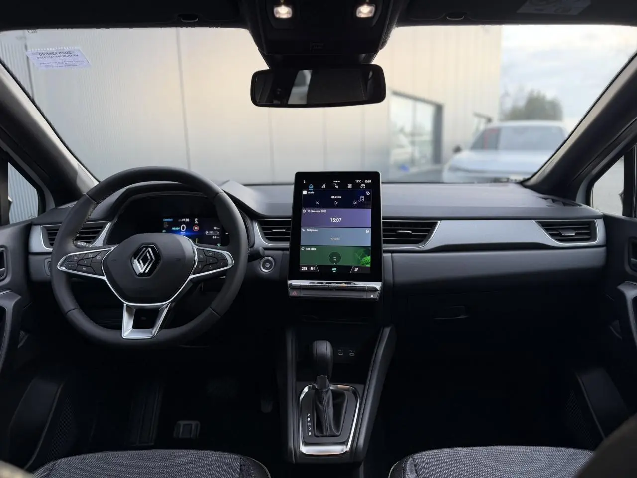 Vue intérieure frontale du tableau de bord du Renault Captur blanc nacré, avec écran tactile vertical et volant multifonction.