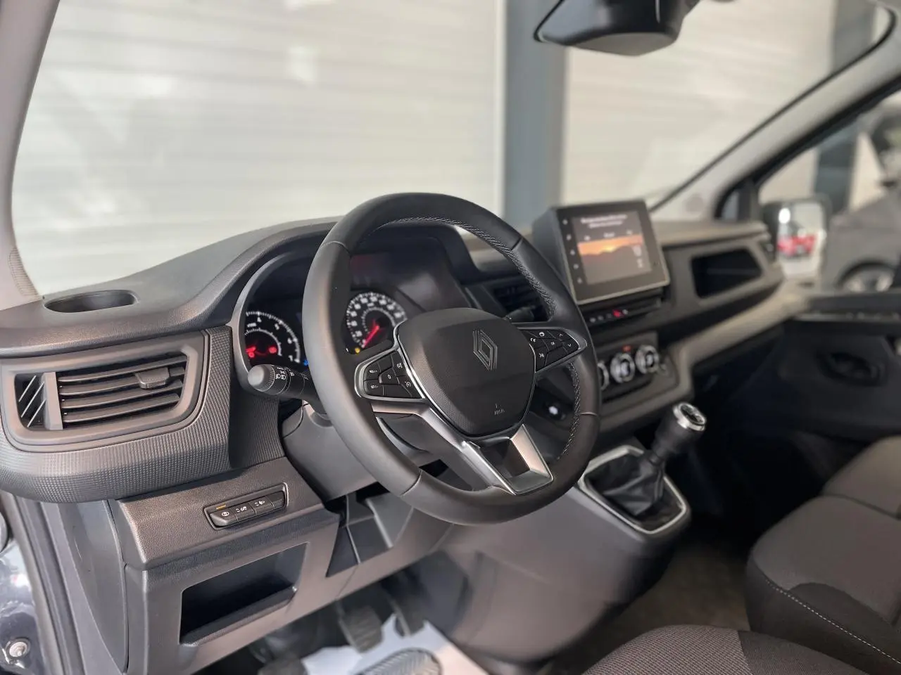 Vue intérieure côté conducteur du Renault Trafic Fourgon gris Comète, avec volant multifonction et écran tactile central.