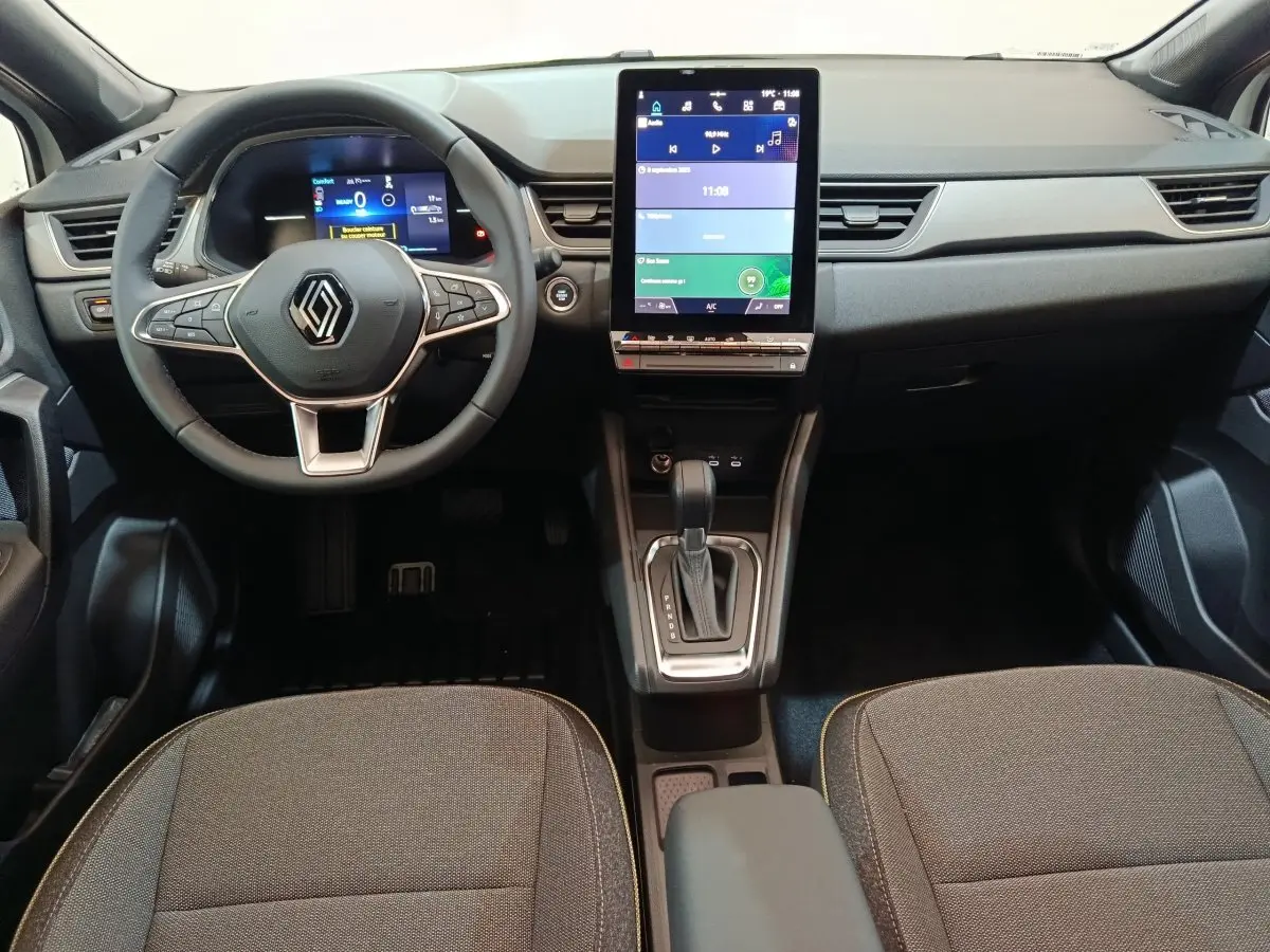 Vue intérieure avant du Renault Captur 2025, tableau de bord avec écran tactile vertical et volant multifonctions en cuir.