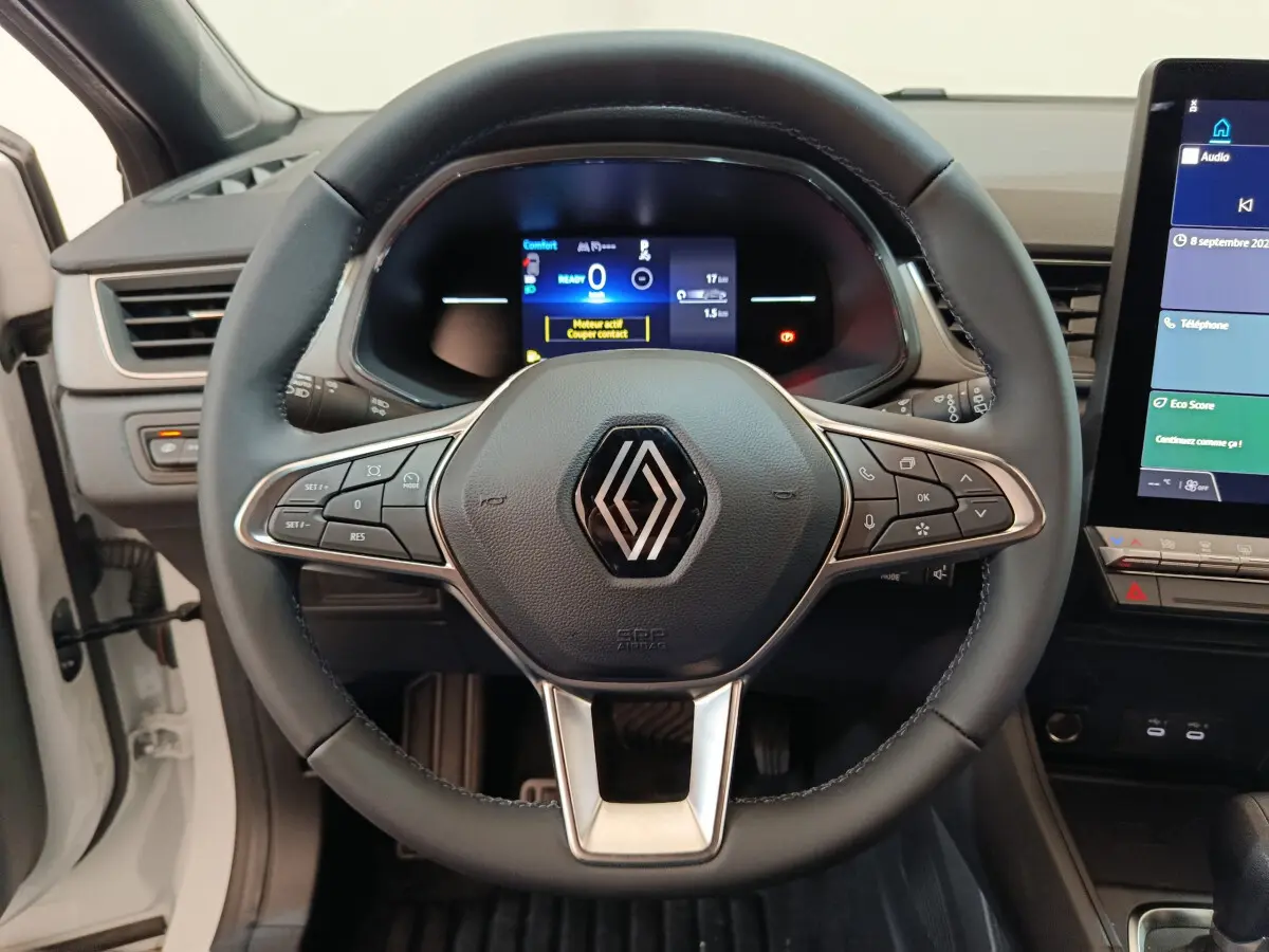 Vue frontale du volant cuir noir avec commandes multifonctions du Renault Captur Techno E-Tech 145 blanc, tableau de bord numérique.