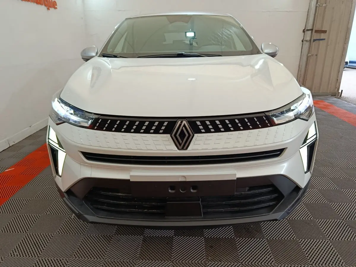 Vue frontale du Renault Captur blanc 2025 avec calandre moderne et phares LED allumés dans un garage.