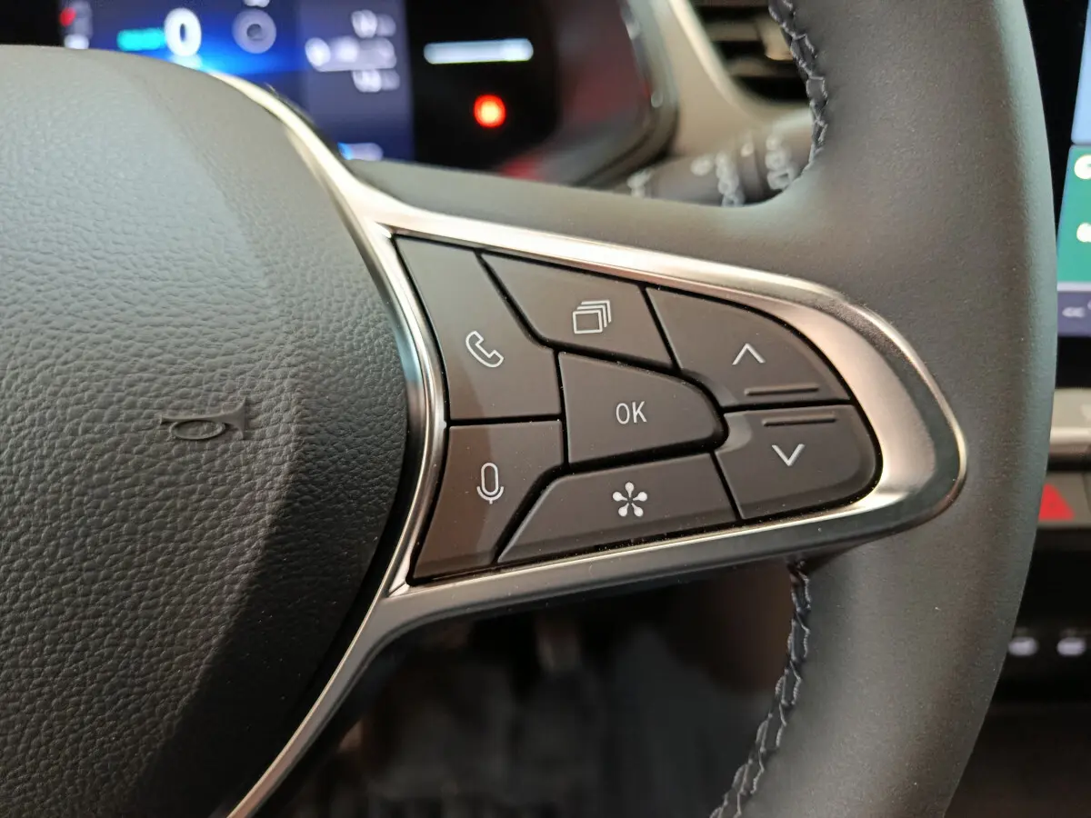 Gros plan sur les commandes multifonctions du volant cuir noir du Renault Captur blanc, version techno E-Tech 2025.