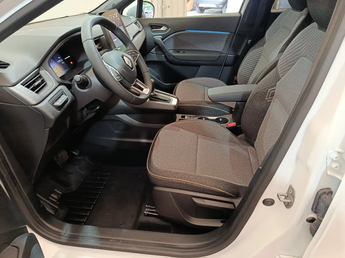 Intérieur avant droit du Renault Captur blanc 2025, sièges tissu gris et tableau de bord avec écran tactile vertical.