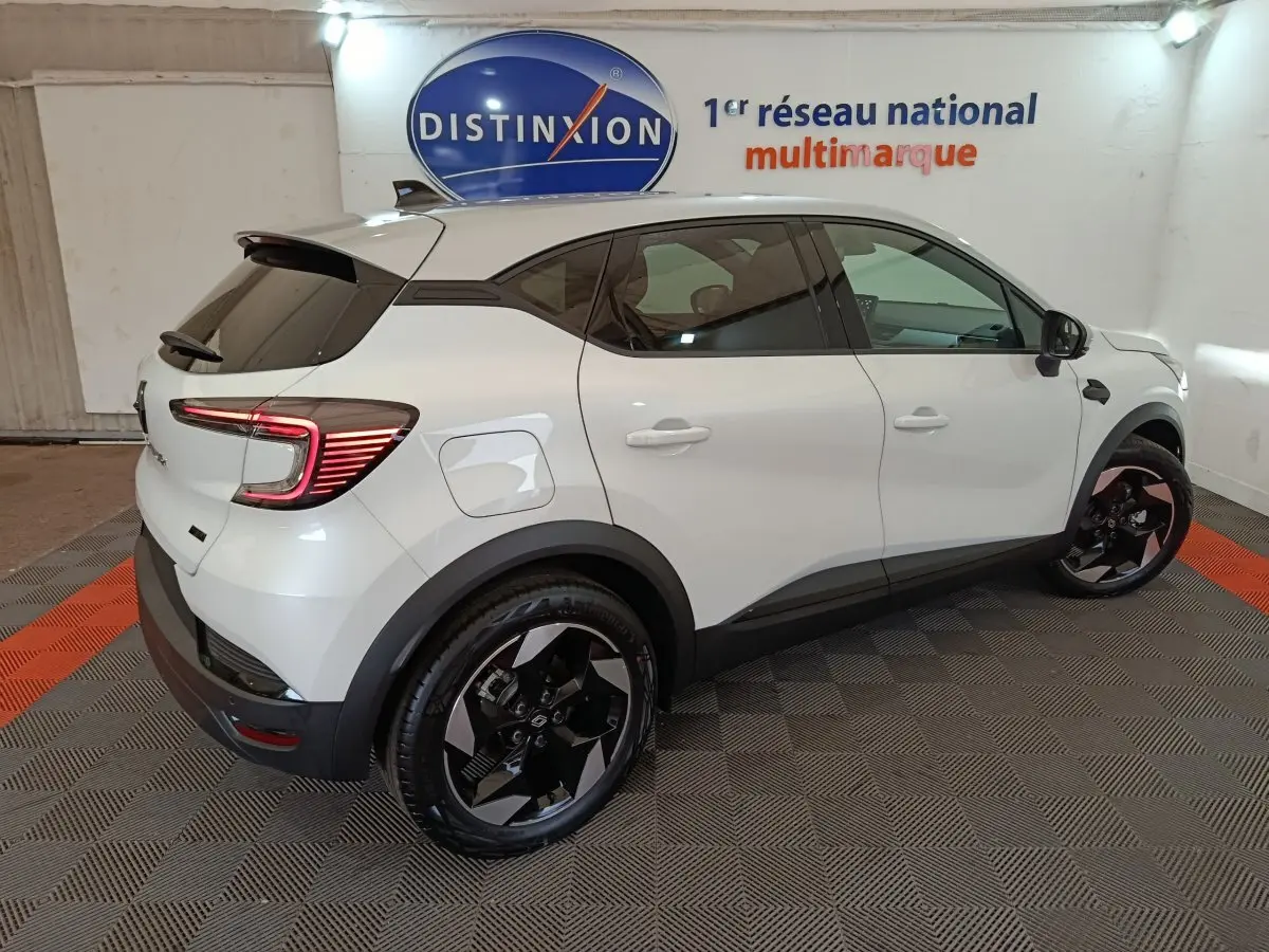 Vue 3/4 arrière droite du Renault Captur Techno E-Tech blanc, avec jantes noires et feux arrière LED allumés.