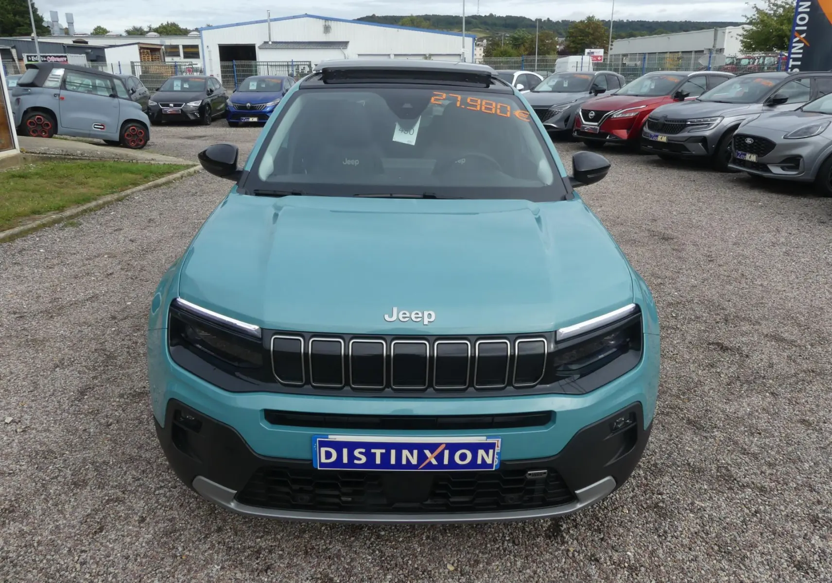 Vue avant d'un Jeep Avenger bleu métallisé 2024 avec calandre noire et plaque Distinxion sur parking.