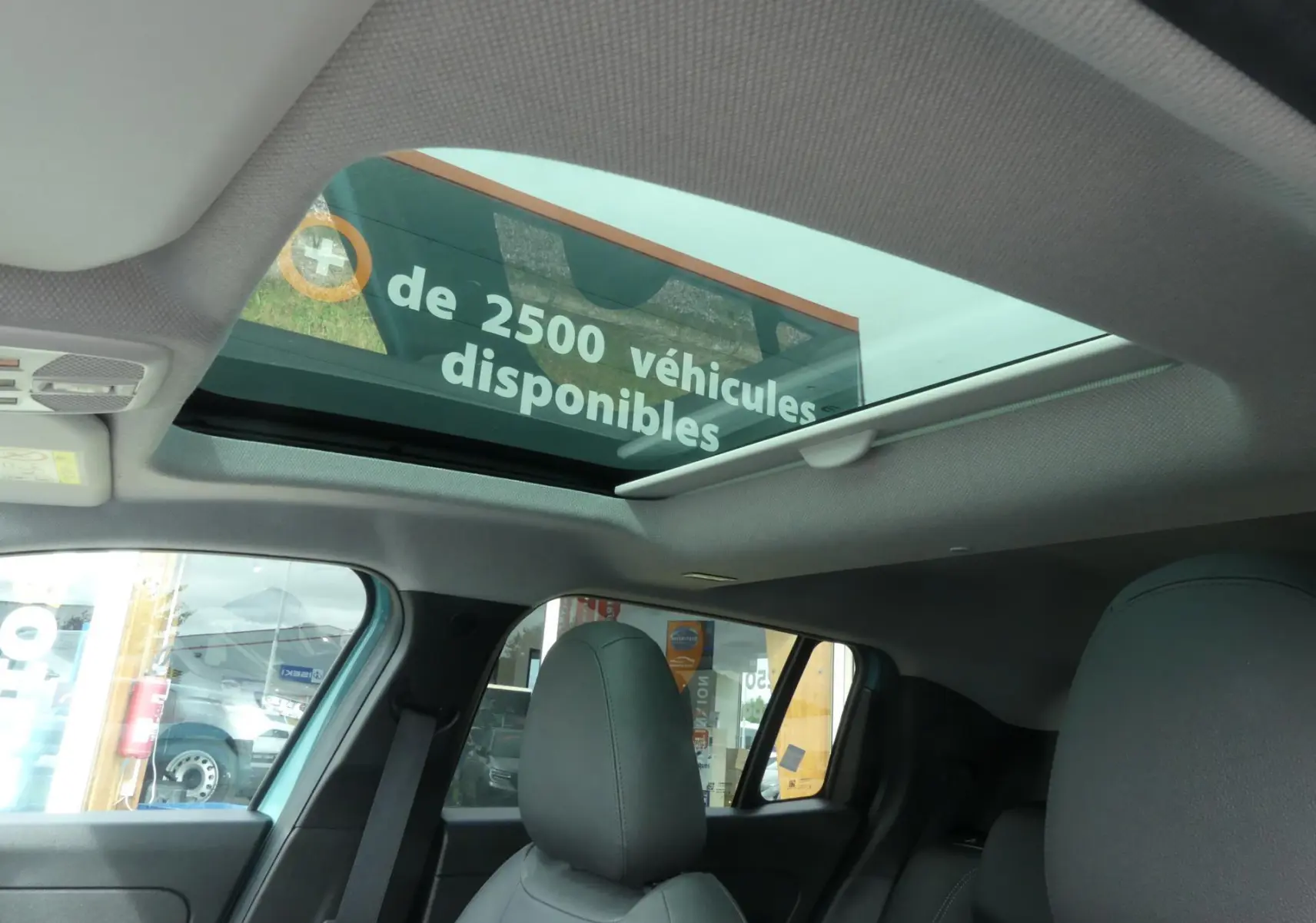 Vue intérieure du toit ouvrant en verre et des sièges avant noirs du Jeep Avenger bleu métallisé 2024.