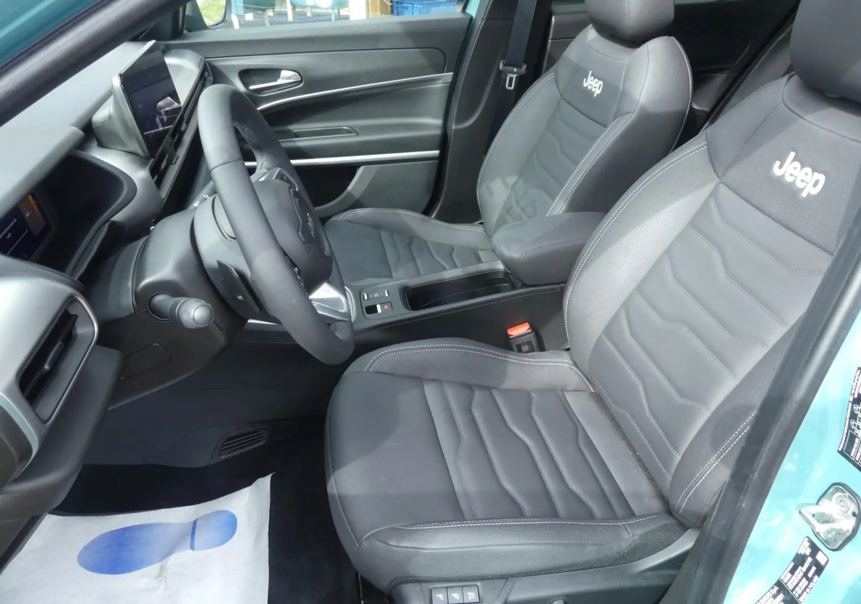 Vue intérieure côté conducteur du Jeep Avenger 2024 bleu métallisé, sièges cuir noir avec logo Jeep brodé.