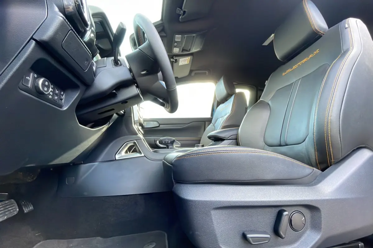 Intérieur côté conducteur du Ford Ranger Wildtrak 2025, sièges cuir noirs avec surpiqûres orange et logo Wildtrak brodé.