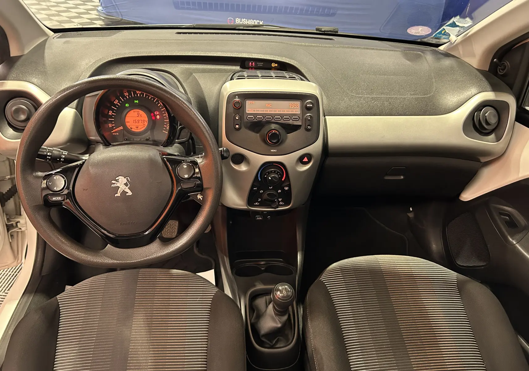 Vue intérieure avant de la Peugeot 108 blanche, montrant le volant, la console centrale avec radio et la boîte manuelle.