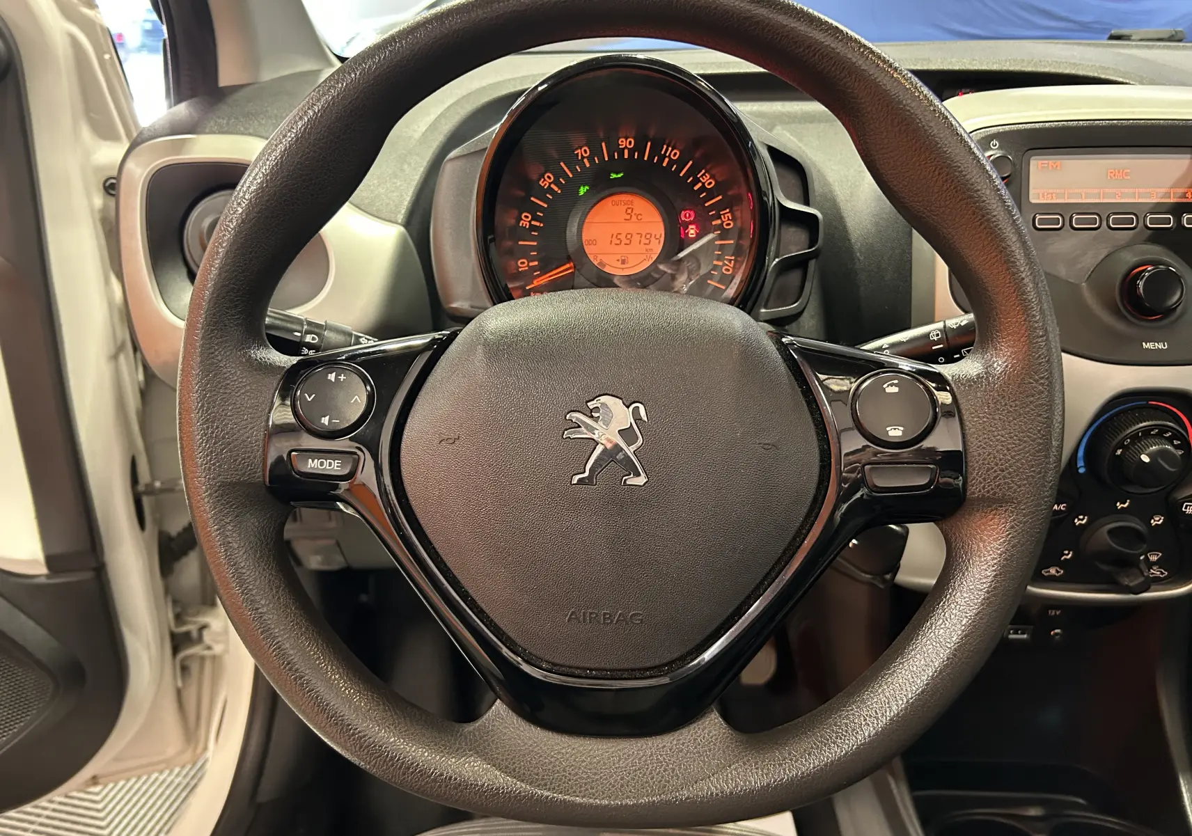 Vue rapprochée du volant noir de la Peugeot 108 blanche de 2014 avec tableau de bord et commandes visibles.