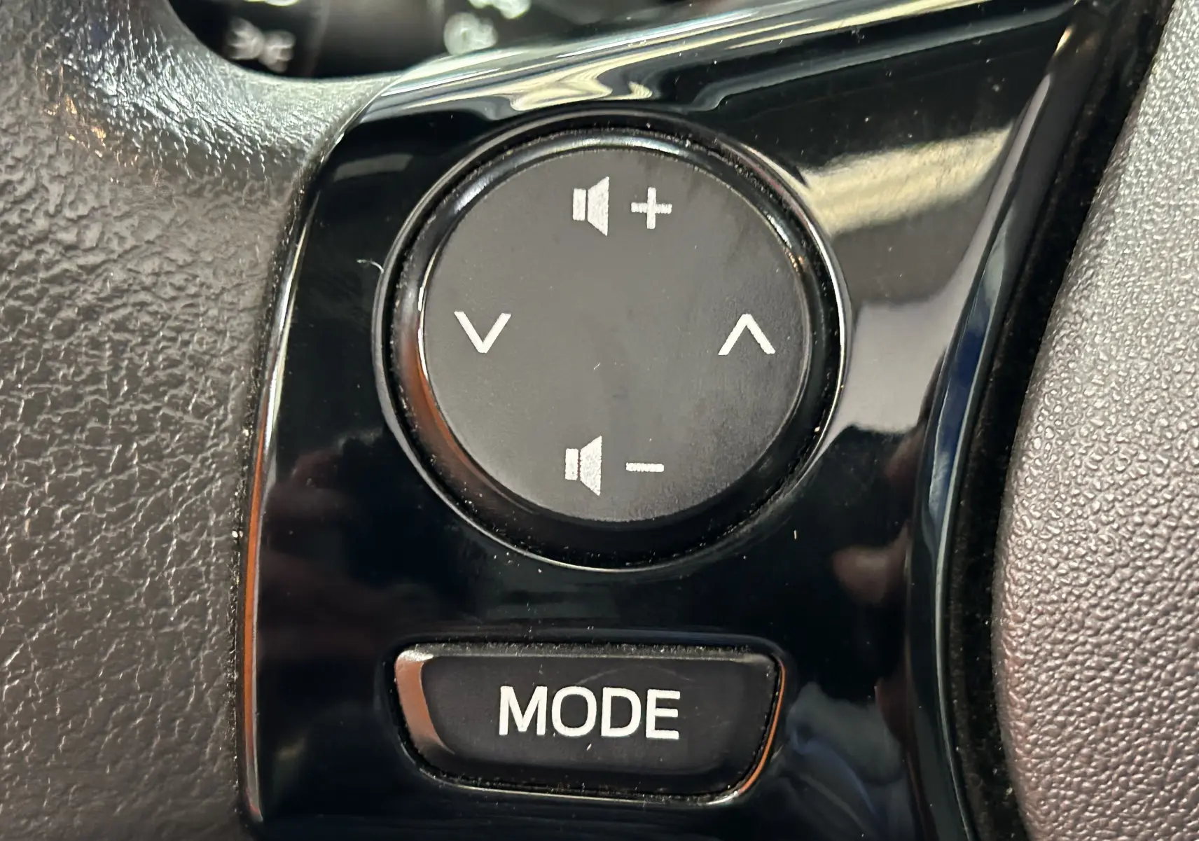 Gros plan sur les commandes audio au volant noir d'une Peugeot 108 blanche, boutons volume et mode visibles.