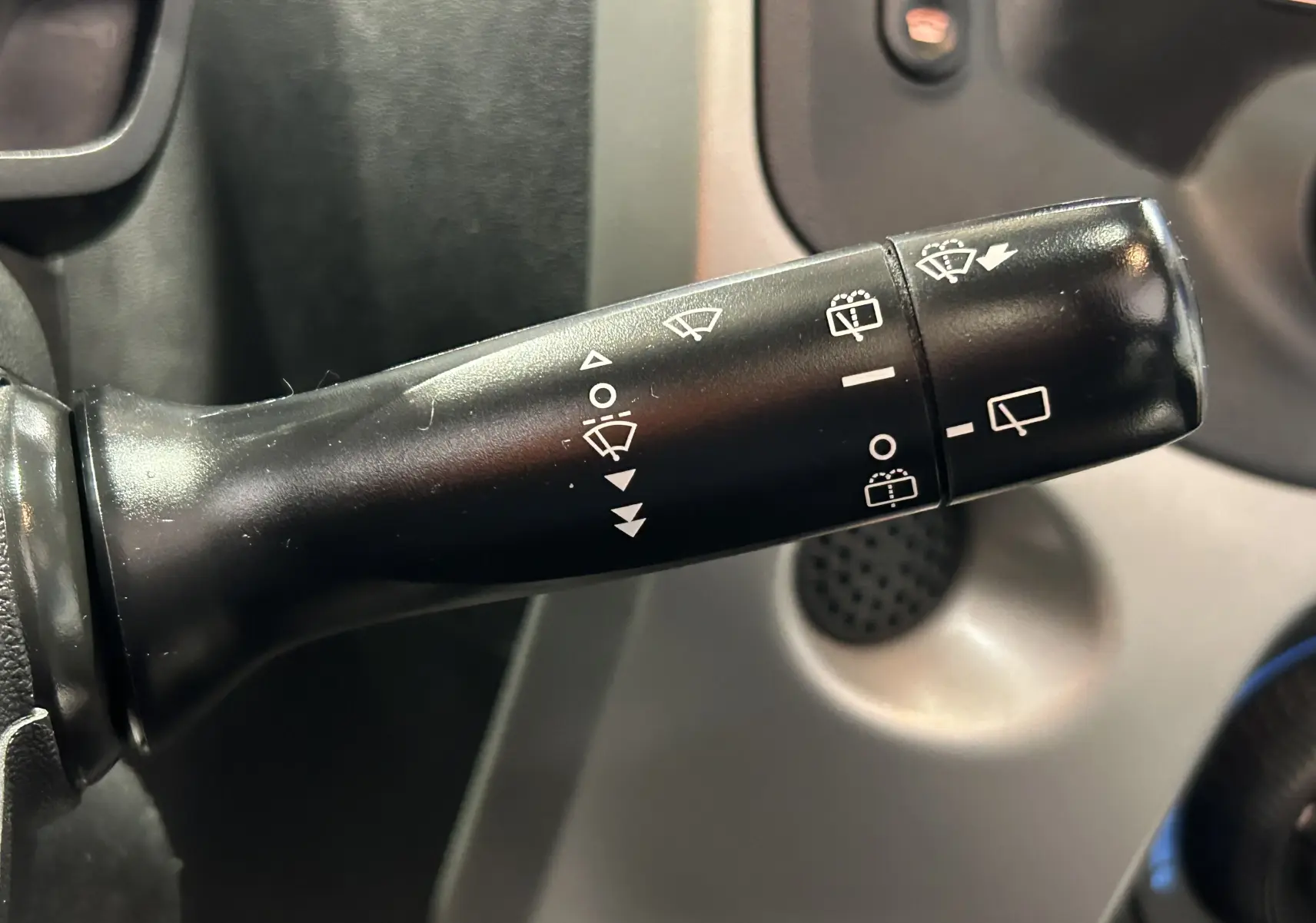 Gros plan sur la manette de commande des essuie-glaces noire dans l'habitacle d'une Peugeot 108 blanche.