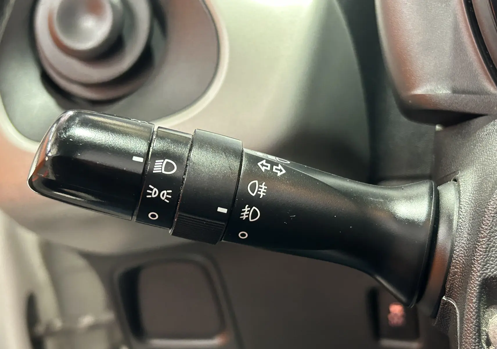 Gros plan sur la commande de phares et clignotants noire à gauche du volant dans une Peugeot 108 blanche de 2014.