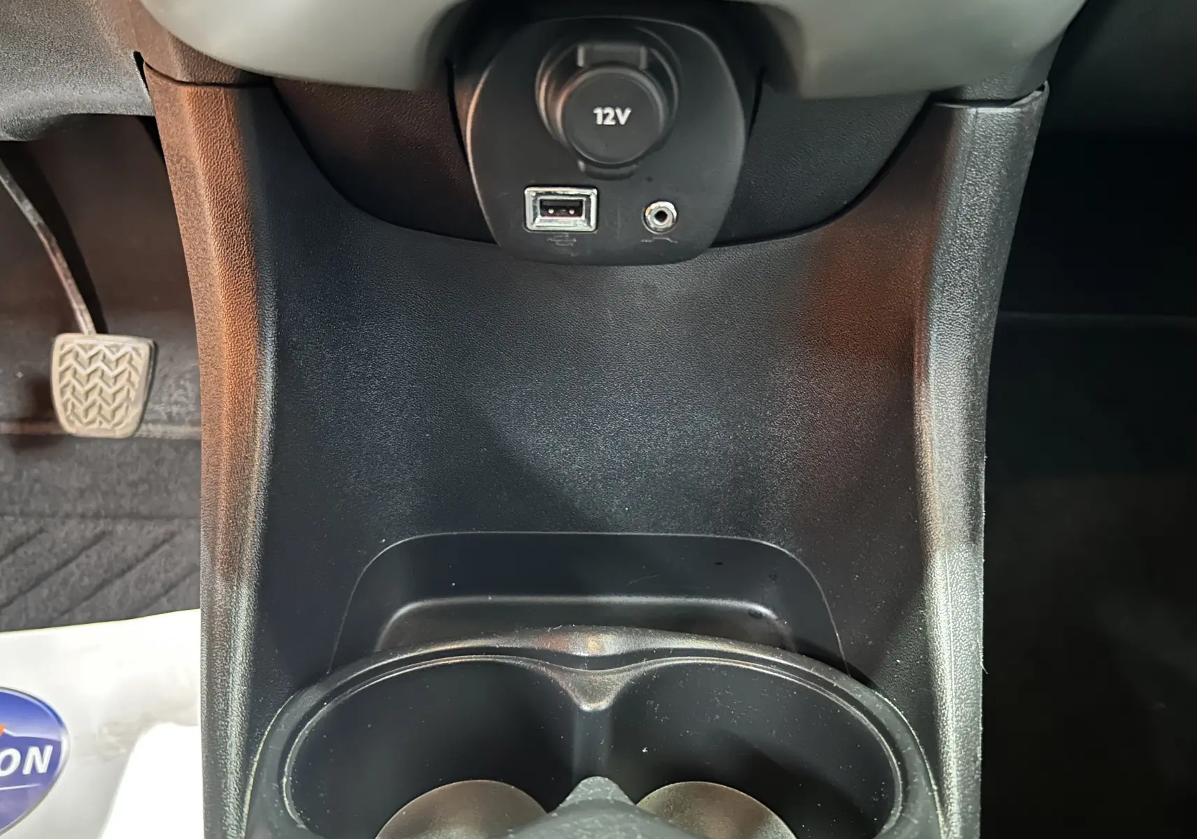 Vue rapprochée de la console centrale noire de la Peugeot 108 avec prise 12V, port USB et prise auxiliaire visibles.