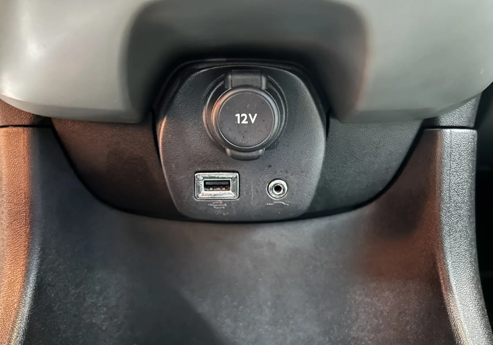 Gros plan sur la prise 12V, port USB et prise auxiliaire du tableau de bord d'une Peugeot 108 blanche.