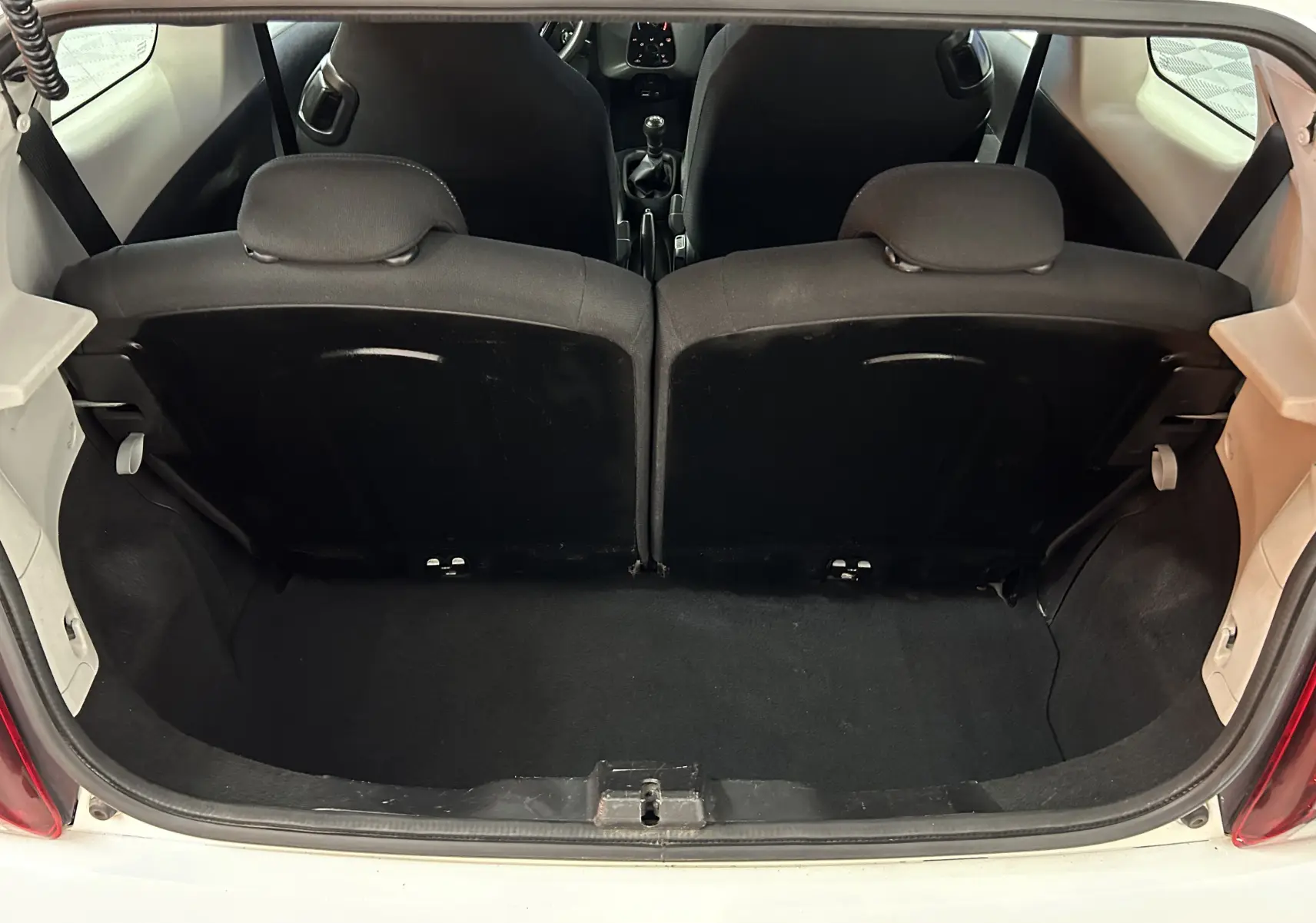 Vue depuis le coffre ouvert d'une Peugeot 108 blanche, montrant l'intérieur noir des sièges arrière et la boîte manuelle.