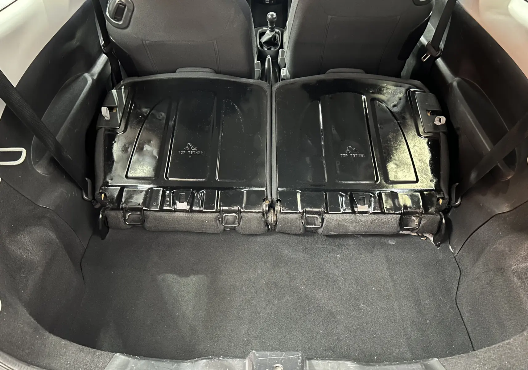 Vue du coffre arrière d'une Peugeot 108 blanche avec banquette arrière rabattue, montrant l'espace de chargement et l'intérieur noir.