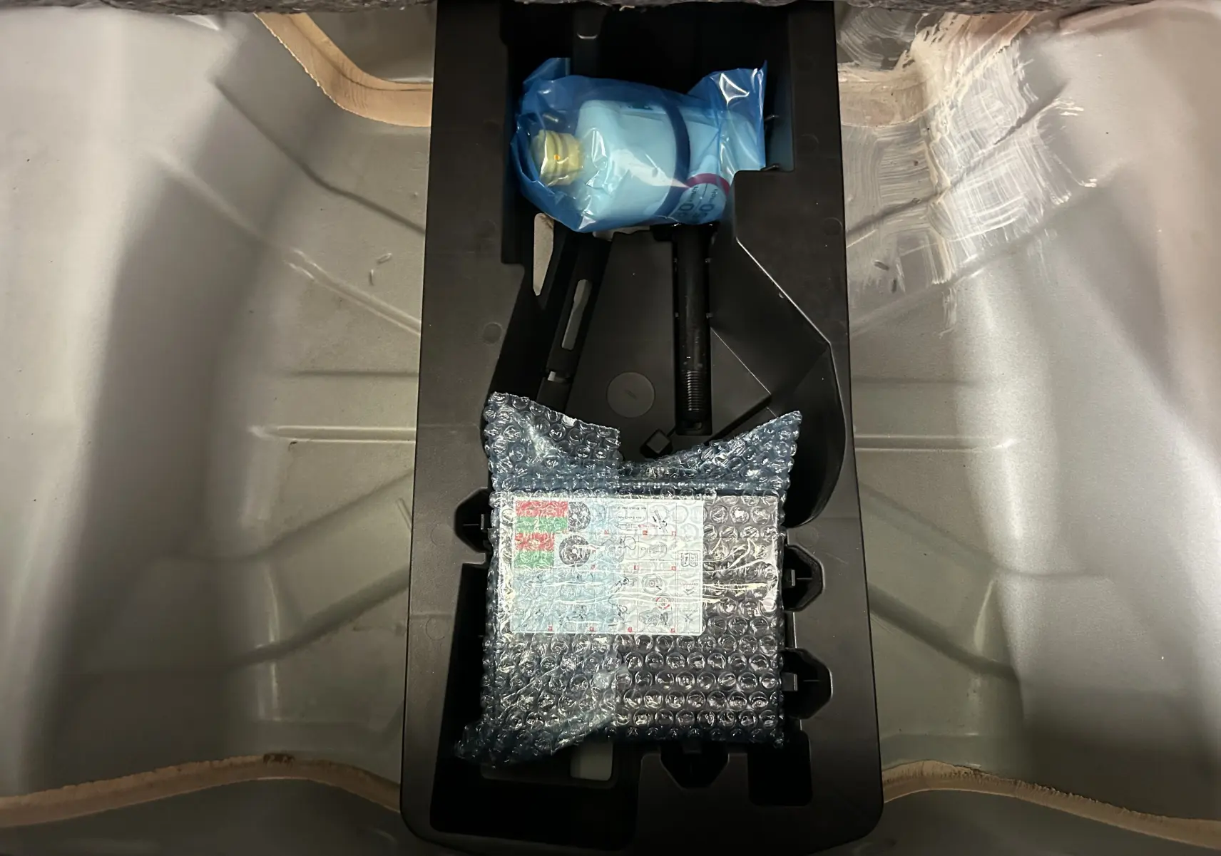 Vue plongeante sur le coffre d’une Peugeot 108 blanc, montrant un rangement avec outils emballés sous plastique et film bulle.